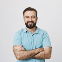 Portrait of a handsome bearded man smiling looking to the camera with his hands crossed isolated on white background. This person looks like an ordinary guy who is sincere and ready to help everyone.